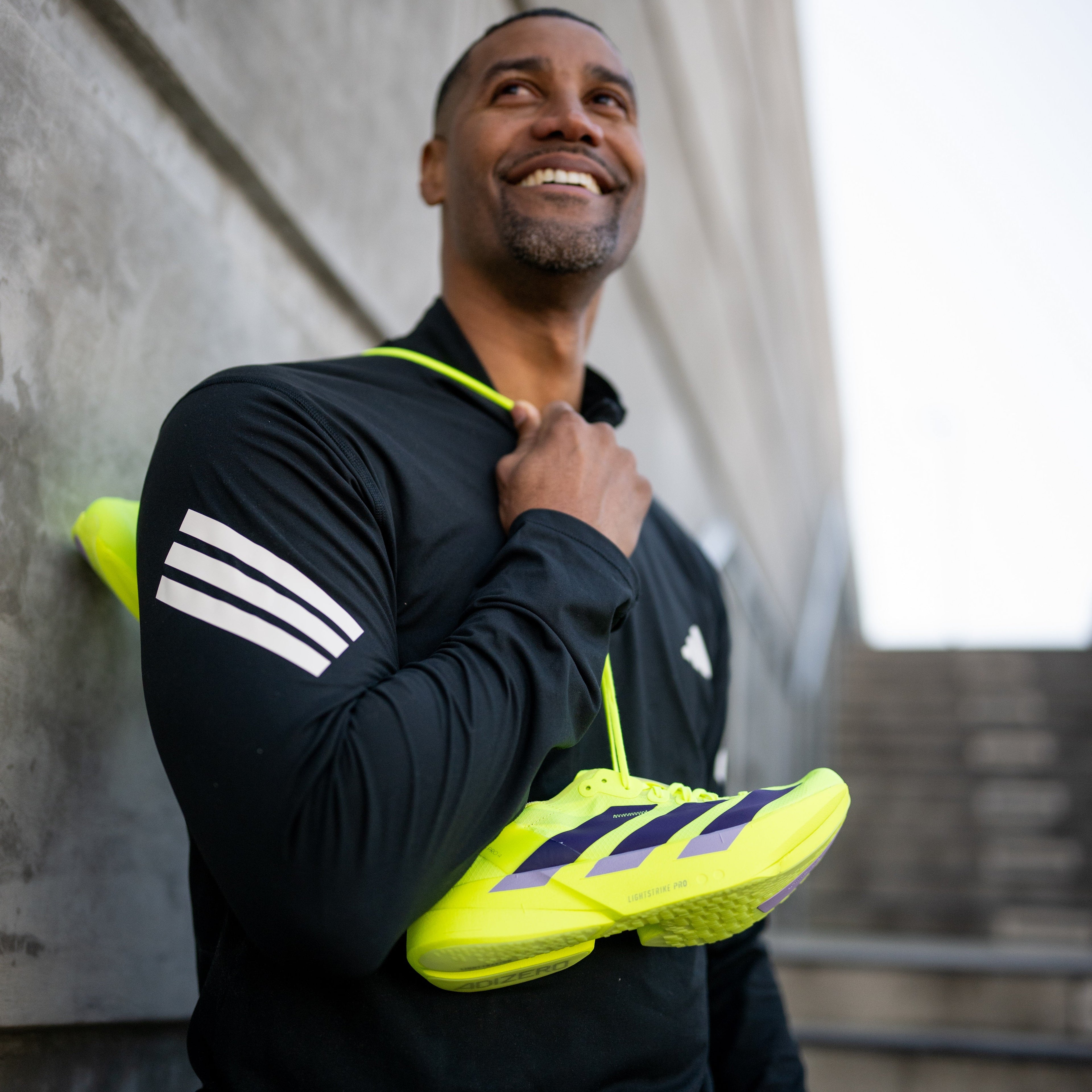 Man holding bright yellow athletic shoes against a gray wall.