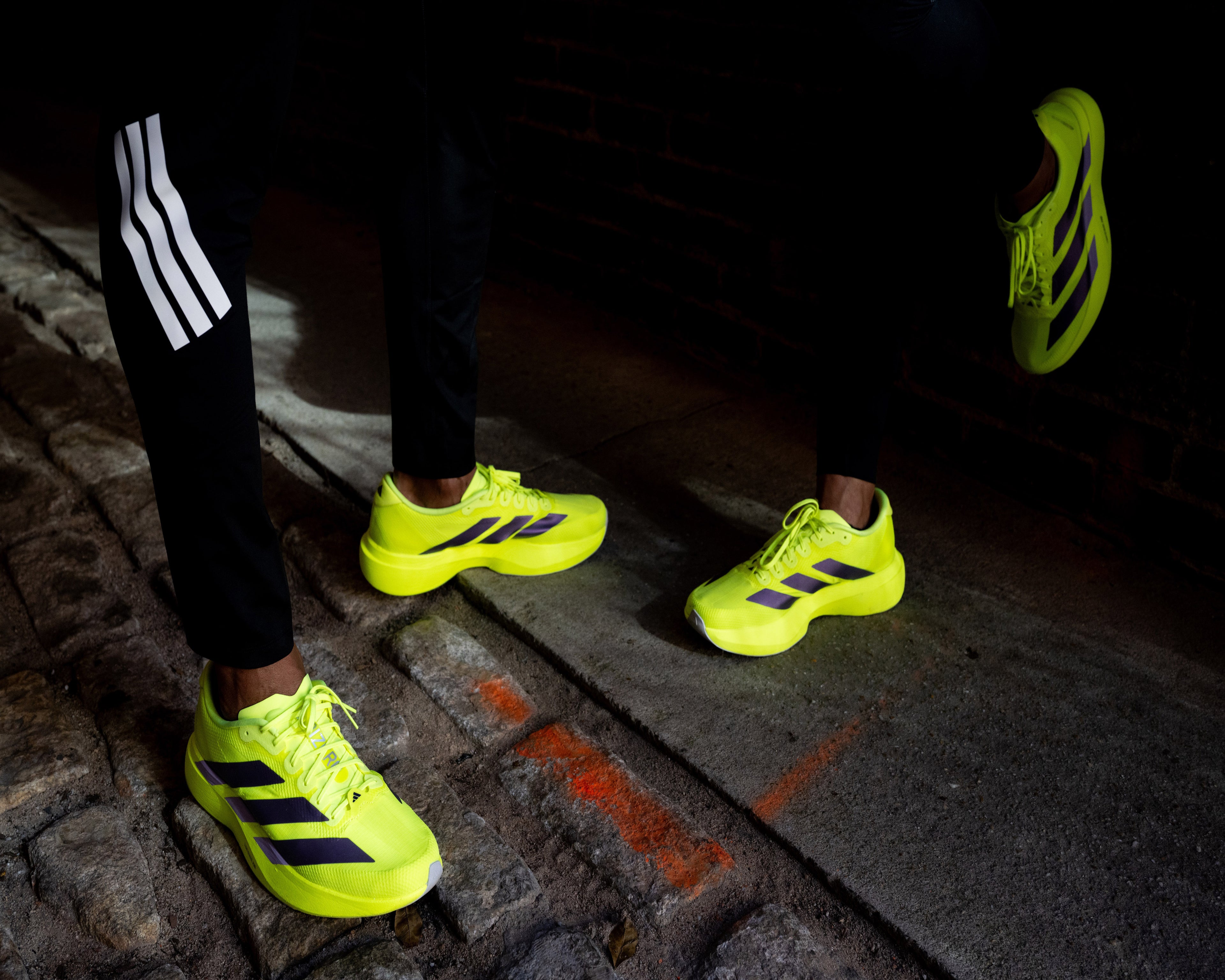 Person wearing bright yellow athletic shoes with black stripes on a dark street.